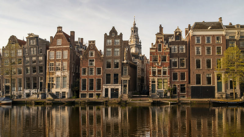 Scheve grachtenpanden aan het Damrak in Amsterdam, bekend als de Dansende Huizen, gezien vanaf de overkant van het water